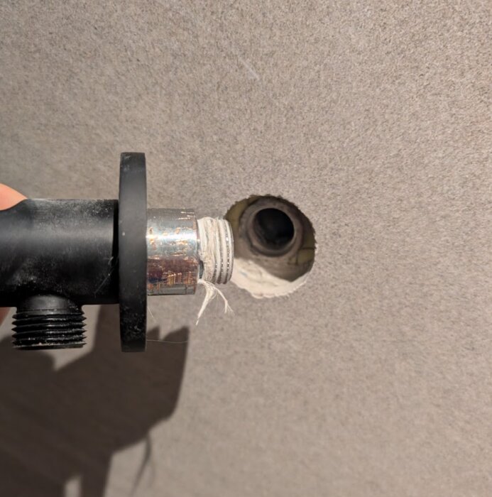 Svart vattenslang med gängtejp vid änden framför kakelvägg med hål för anslutning av dusch.