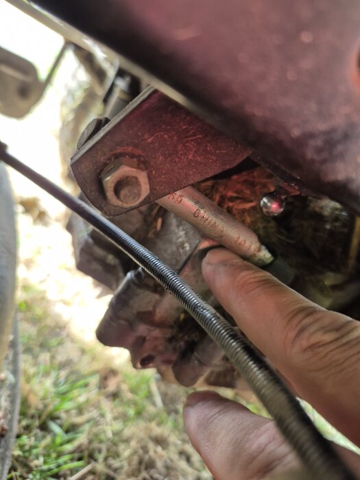 Person pekar på trasig del nära växellåda på maskin, svår att identifiera men verkar lätt att byta ut.