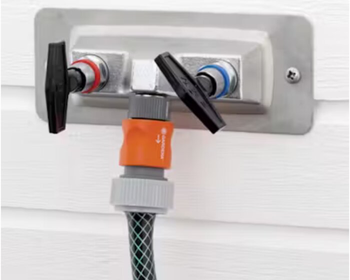 Utomhus vattenanslutning med varm- och kallvattenkranar och en ansluten trädgårdsslang.