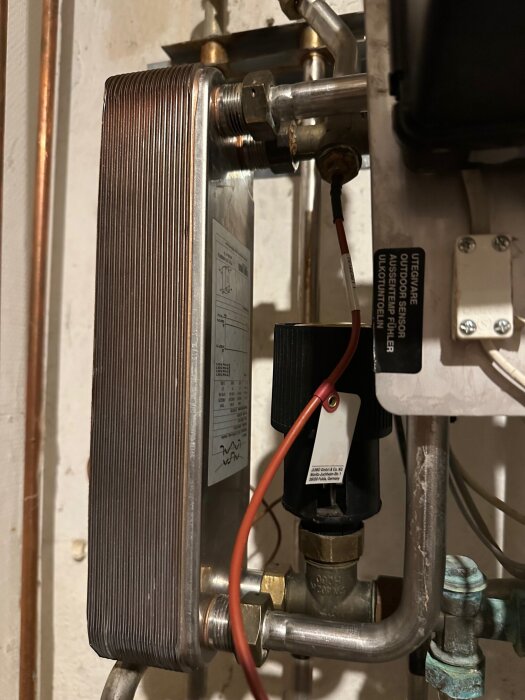En värmeväxlare med kopparrör och en installerad regulator i en bygganläggning, samt anslutna ledningar och ventiler.