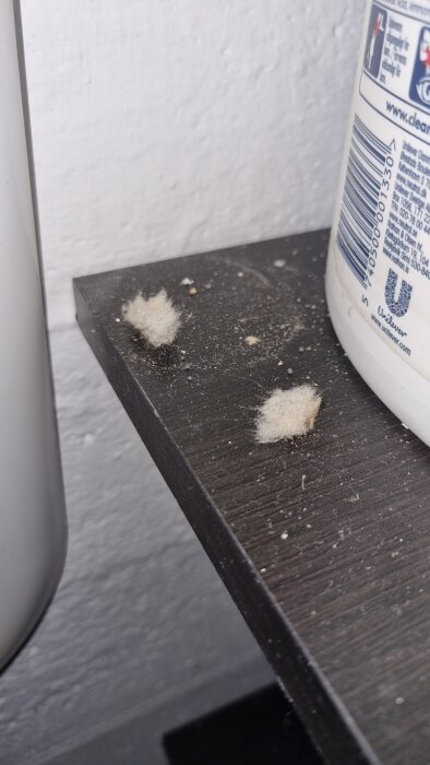 Tussar av vit och brun isoleringsmaterial på en svart hylla nära en plastbehållare.