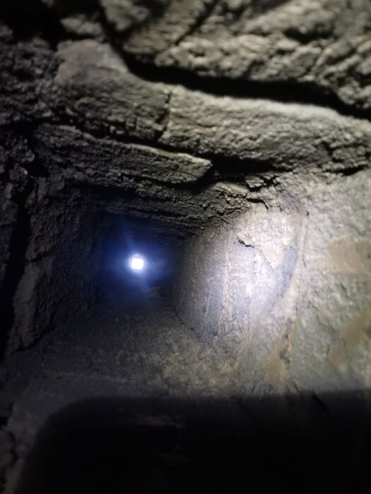 Insida av en smutsig murad kanal eller rökkanal, sedd nerifrån och uppåt mot ett ljus i slutet av kanalen.