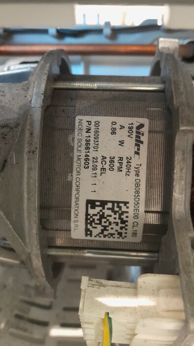 Motor med etikett från en torktumlare med specifikationer, inklusive Nidec-märke och serienummer, delvis synlig kabelanslutning i förgrunden.