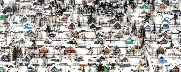Färgglada hus i ett snötäckt landskap med träd och skog i bakgrunden.