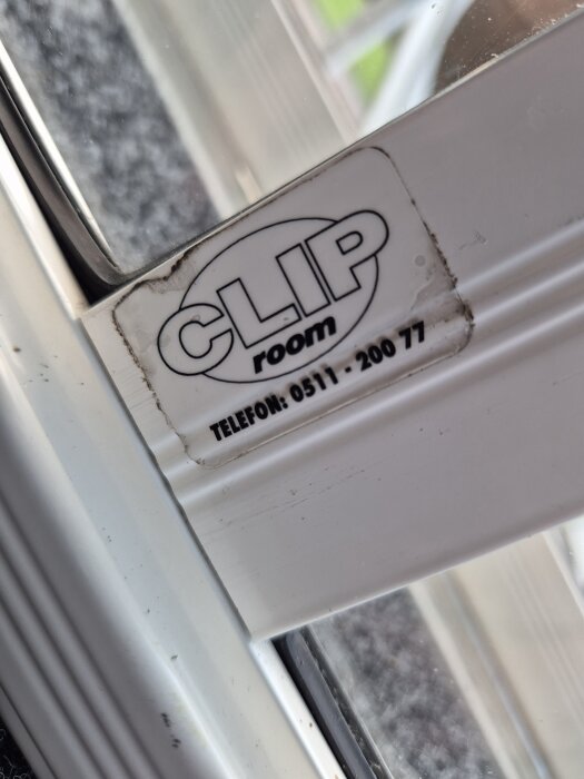 Fönsterkarm med etikett "CLIP room" och ett telefonnummer, delvis suddig bakgrund.