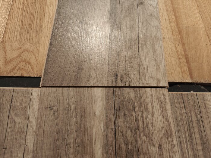 Laminatgolv ligger ovanpå gammal ekparkett, visar jämförelse mellan de två golvtyperna och deras skilda texturer och färger.