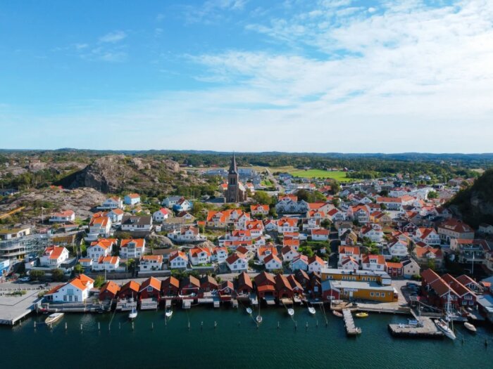 En pittoresk kuststad med färgglada hus och en kyrka, omgiven av berg och hav, som visar traditionell arkitektur utan moderna detaljplaner.