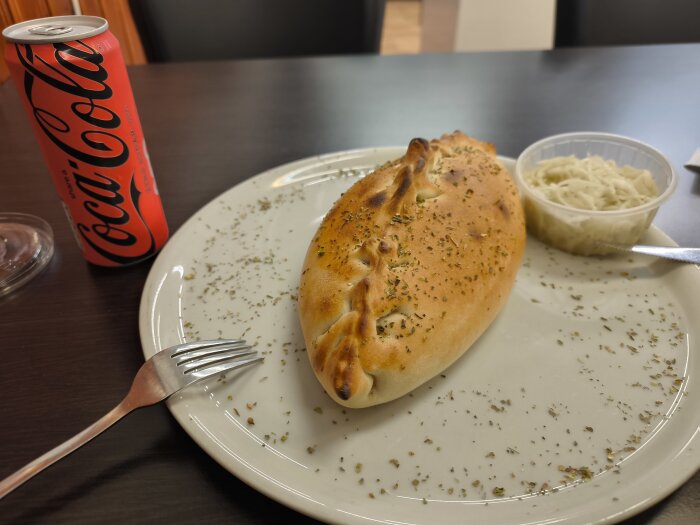 Calzone med örter på tallrik, bredvid Coca-Cola-burk och liten skål med coleslaw.