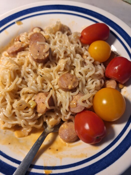 Tallrik med snabbnudlar och stroganoff toppad med korvskivor, omgiven av körsbärstomater, på ett bord med gaffel i.