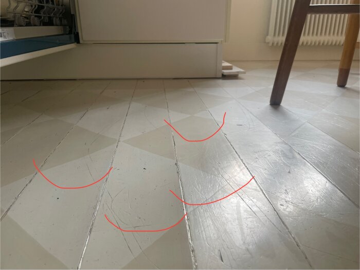 Trägolv med markerade bågformade upphöjningar, tecken på att golvet rest sig. Kombinerat med möbler och kökets inredning i bakgrunden.