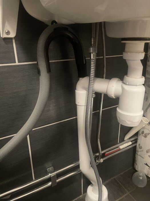 Avloppsrör och slangar under ett handfat i ett badrum, med möjlighet att ansluta en tvättmaskin.