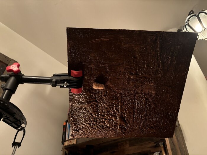 Cykelmekställ håller upp en mörkbemålad plywoodskiva med en fastlimmad kork, underifrån testas limstyrkan för bastuförhållanden.