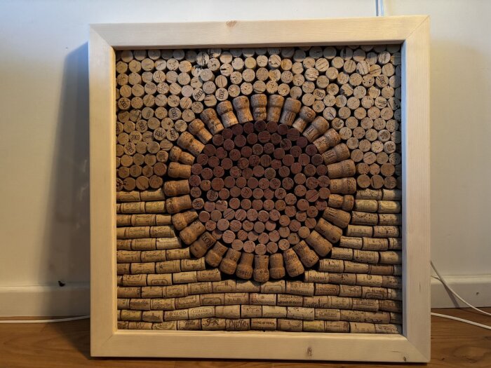 Inramad konstverk av vinkorkar arrangerade i cirkelform med varierande färger, upphängd som test i bastumiljö för hållbarhet.