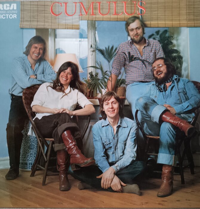 En grupp människor sitter och står avslappnat framför en inomhusväxt, med ordet "Cumulus" ovanför dem.