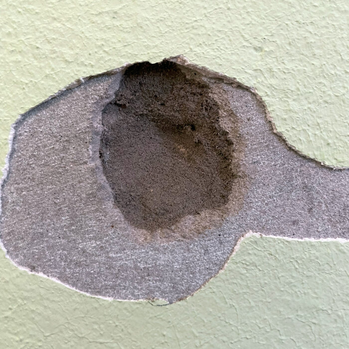 Vägg med grönt målat spackel och lager av cementputs, avslöjar ett mörkgrått, smuligt inre material.