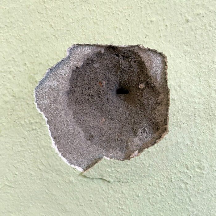 Närbild på en vägg där färglager och cementputs har skrapats bort, avslöjande ett mörkgrått, smuligt material innanför.