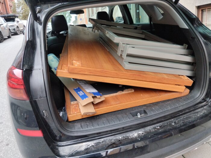 Tre stora träbordsskivor och metallben lastade i bagageutrymmet på en svart bil.