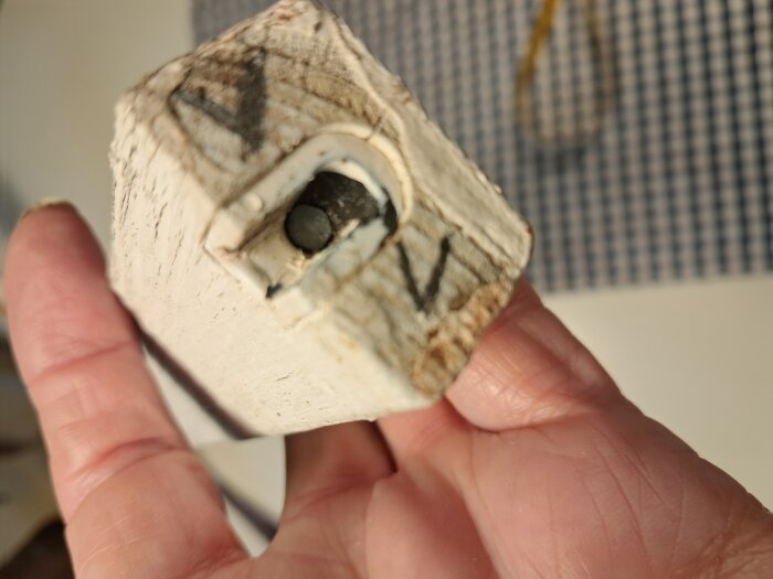 Hand håller i ett trästycke med inbyggd metallbeslag, visande ett enkelt fäste med spik för fönsterspröjs.