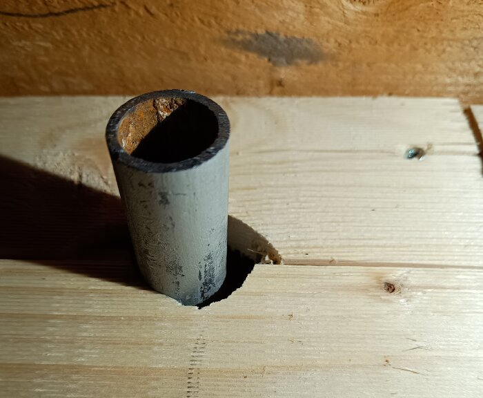 Rör som går igenom en grovt utskuren öppning i ett träplank på ett vindsgolv efter en vattenskada.