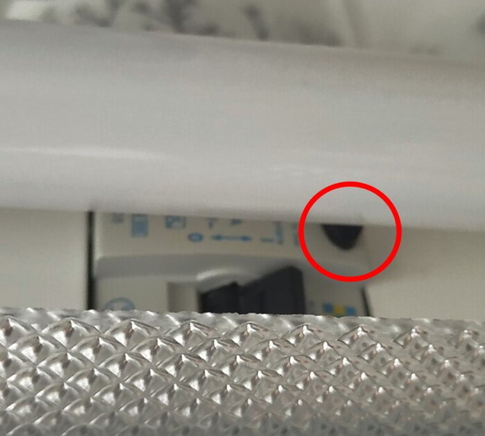 Bild på en jordfelsbrytare i ett skåp med ett lysrör ovanför. En svart knapp är markerad med en röd cirkel som troligen är testknappen.