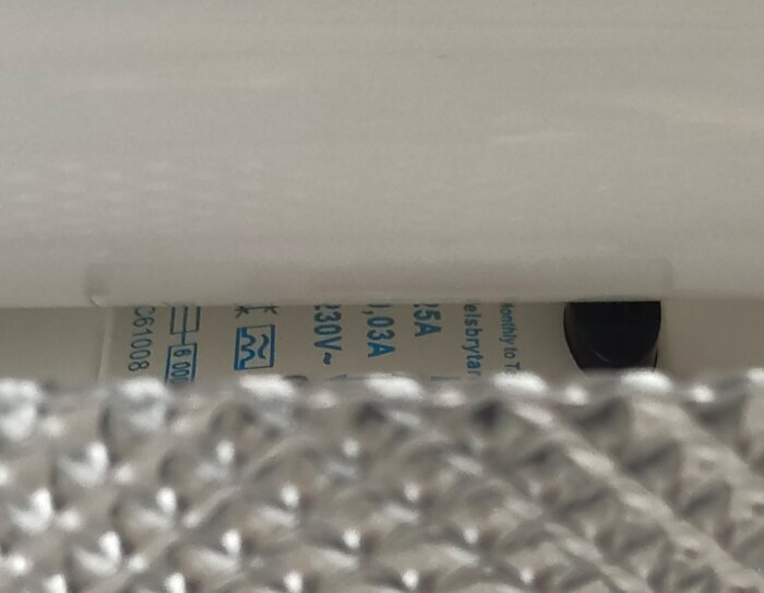 Bild på elektrisk komponent med märkningar och en svart knapp under ett lysrör.