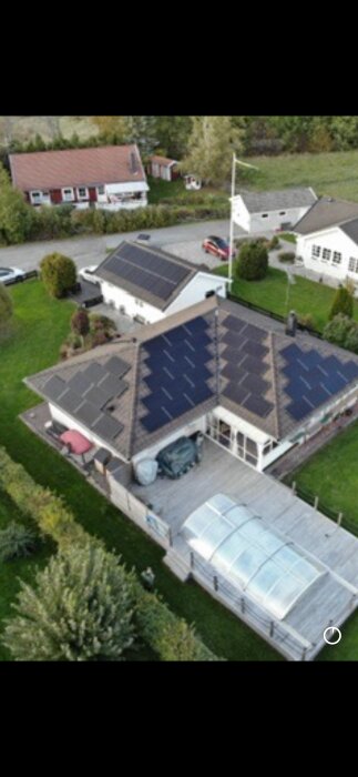 Luftfoto av ett hus med flera solpaneler på taket och garage i ett grönskande bostadsområde.