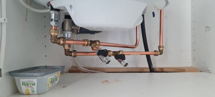 Rörsystem med avtappningsventiler under en diskho i ett köksskåp.