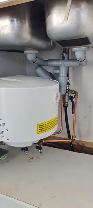 Vattenberedare under diskbänk med avloppsrör och kopparrör.