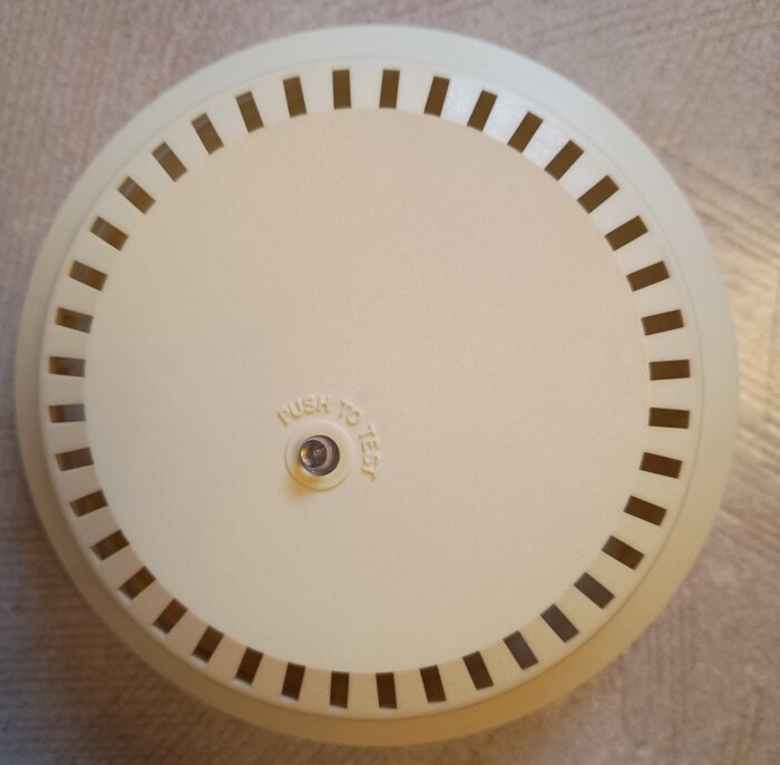 Äldre brandvarnare med knappen "Push to Test" på en beige bakgrund.