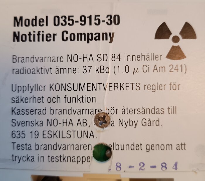 Etikett på en gammal brandvarnare NO-HA SD 84 med radioaktivt ämne, instruktioner för kassering och återvinning, tillverkad av Notifier Company.