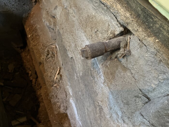 Rostigt rör med plugg i en gammal betongvägg i en krypgrund, del av ett avtappningssystem.