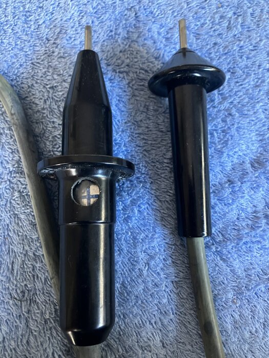 Svarta plastkontakter med metallspetsar på en blå handduk.