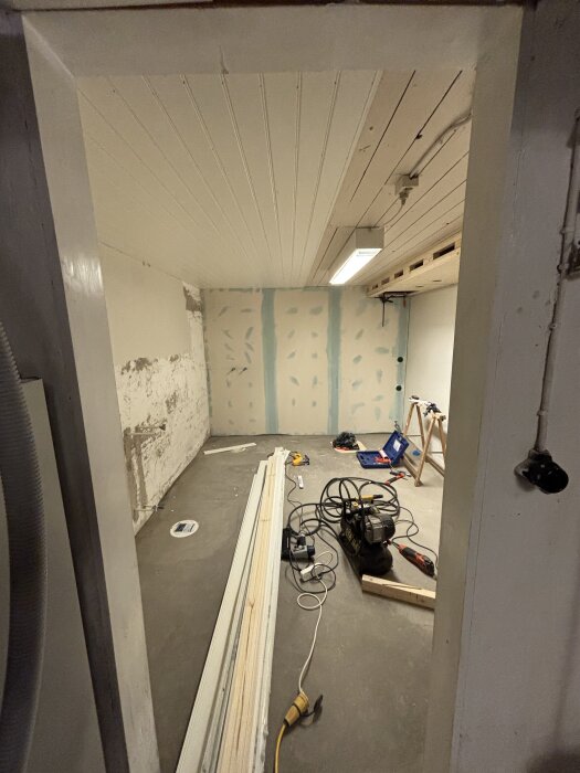 Rum under takrenovering med pärlspont och hålkälslister. Byggmaterial och verktyg spridda på golvet.