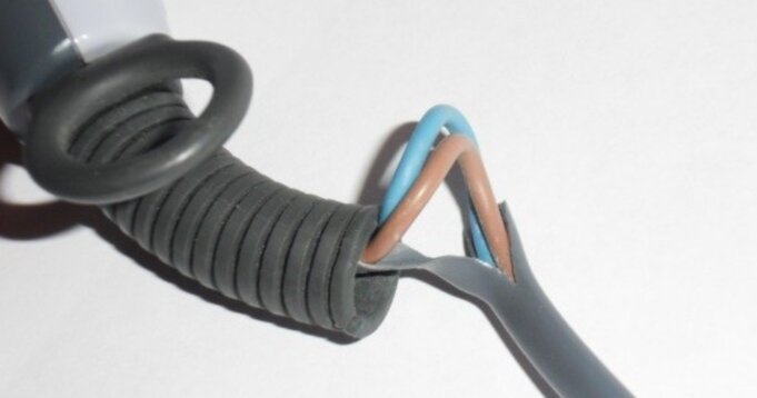 Exponerade kablar med insida synlig, delvis skadad plastisolering på elkabel med blå och brun tråd bredvid en svart spiralformad kabel.