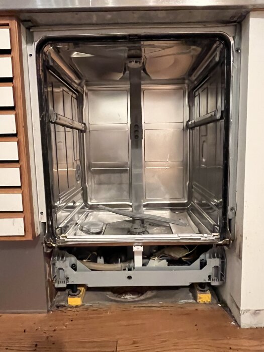 Öppen och tom diskmaskin med exponerade innerväggar och golv, montering synlig, installerad i köksskåp.