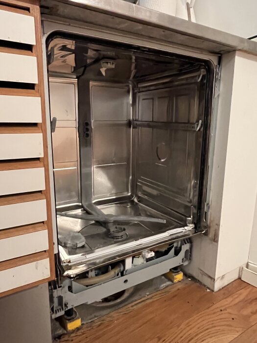 Öppen integrerad diskmaskin under installation, synlig från framsidan med dörr och inredning borttagen, visar sökande efter fastsättning på höger sida.