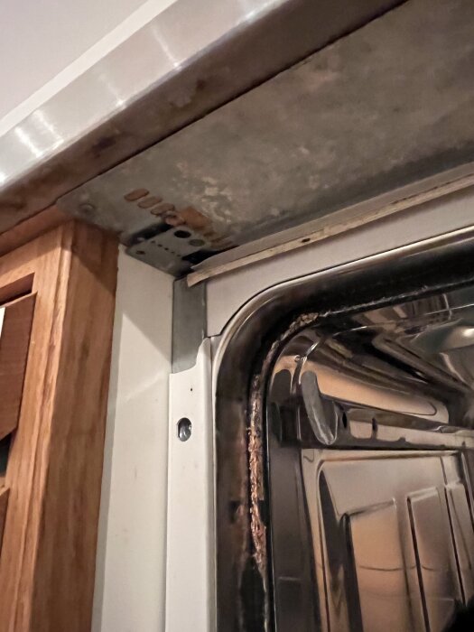 Inbyggd diskmaskin med synligt metalldetalj och anslutning till köksinredning, där höger sida verkar sitta fast.