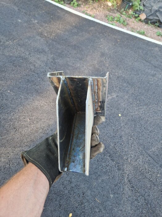 En person med handskar håller en specialdesignad balksko av metall framför asfalt.