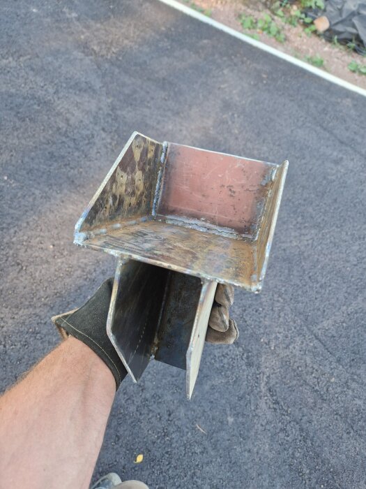 Person i arbetshandske håller en specialdesignad och rostig balksko av metall på en asfalterad yta.