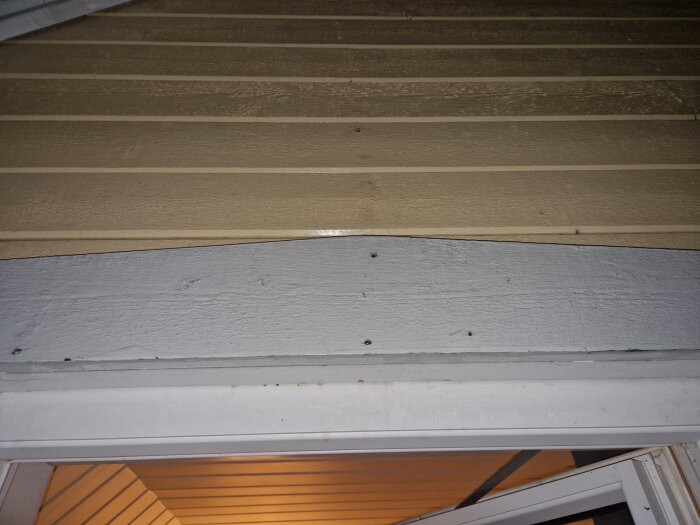 Trätak i ett hus med horisontella ribbor och en vit dörrkarm.