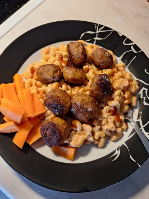 Tallrik med stuvade makaroner, köttbullar och skivade morötter.