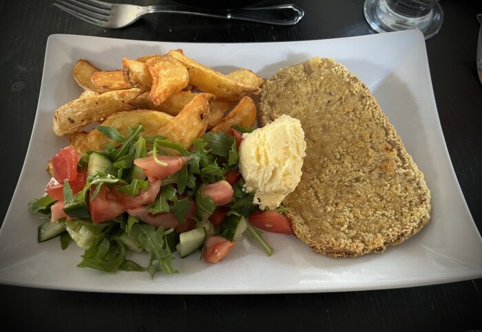 Tallrik med schnitzel, klyftpotatis, vitlökssmör och sallad.
