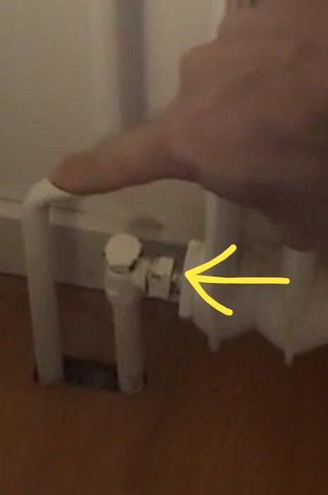 Hand pekar på glipa vid röranslutning till element, med gul pil som visar platsen.