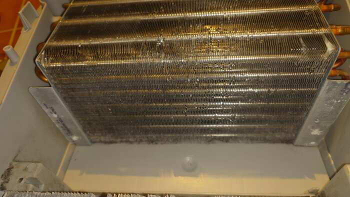 Värmeelementet bakom kondenorn i en Bosch Serie 8, blockerat av smuts och ludd, demonterat för rengöring.
