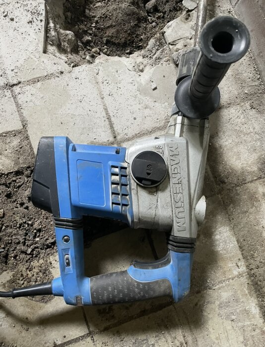 Bilningshammare med blått handtag ligger på en delvis bruten betonggolvyta.