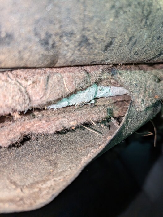 Skadad isolering på rör i en krypgrund, troligen angripen av skadedjur och eventuellt innehållande asbest.