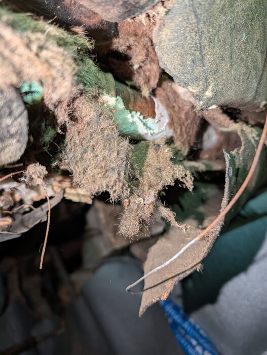 Skadad isolering runt rör i en krypgrund, potentiellt asbest, med delvis blottade rör och fragment av material runtomkring.