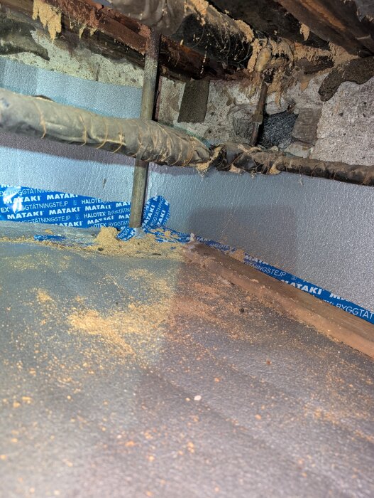 Rör i krypgrund med skadad isolering, möjligen orsakad av skadedjur, med blå tejprester synliga i bakgrunden.