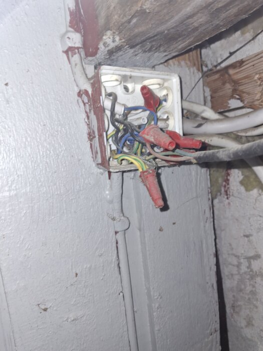 Gammal elinstallation med synliga kablar i en kopplingsdosa, gul/gröna jorden finns med, frågetecken kring andra färgers funktion.