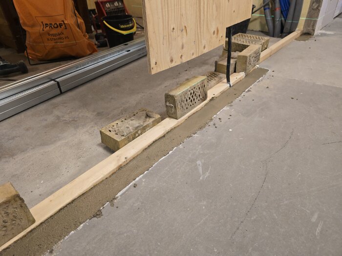 Betonggolv med träregel och tegelstenar för innerväggbyggande, sett i ett renoveringsprojekt. Spikplugg och fogmassa används för att skapa en tät vägg.